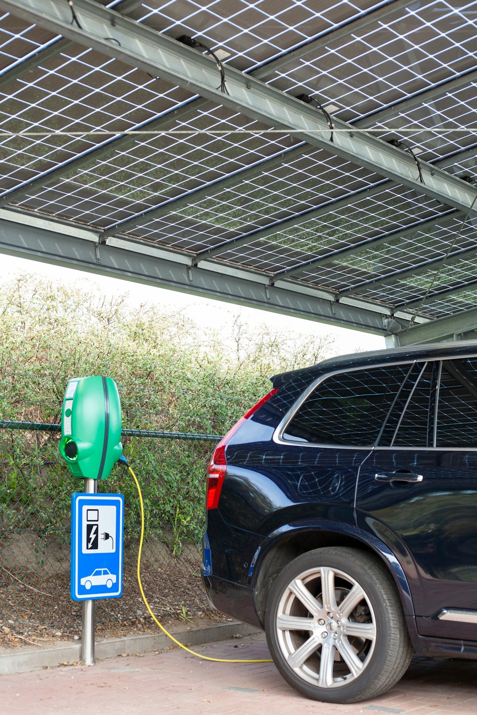 Camioneta SUV azul oscuro cargando en una estación de vehículos eléctricos verde bajo paneles solares.