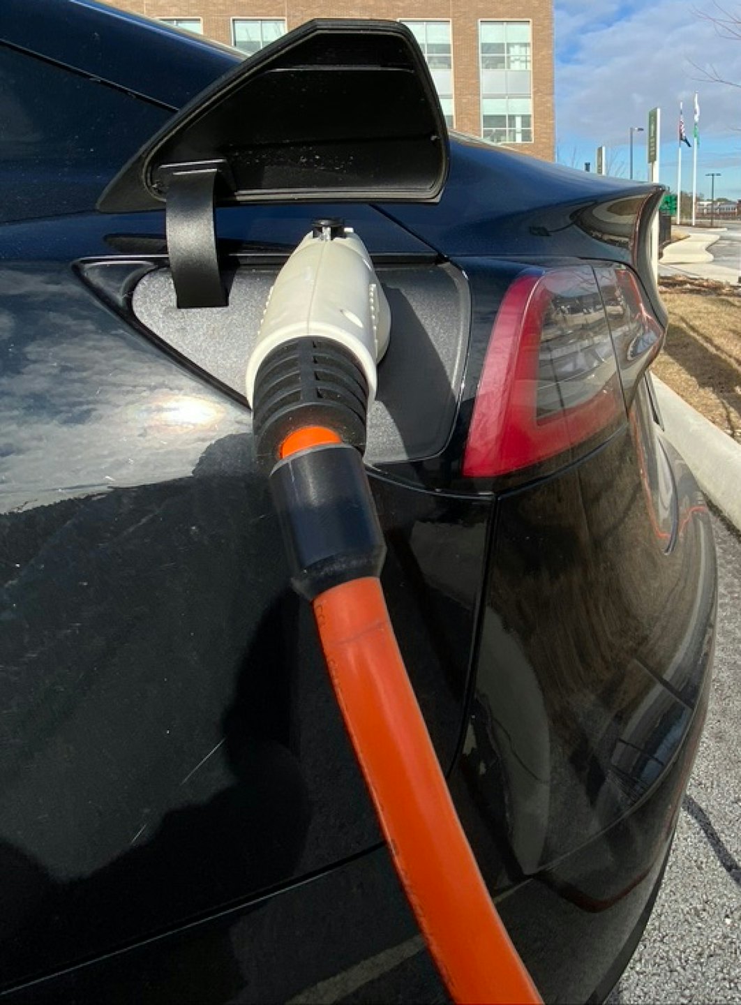 Coche eléctrico negro cargando al aire libre con cable naranja.