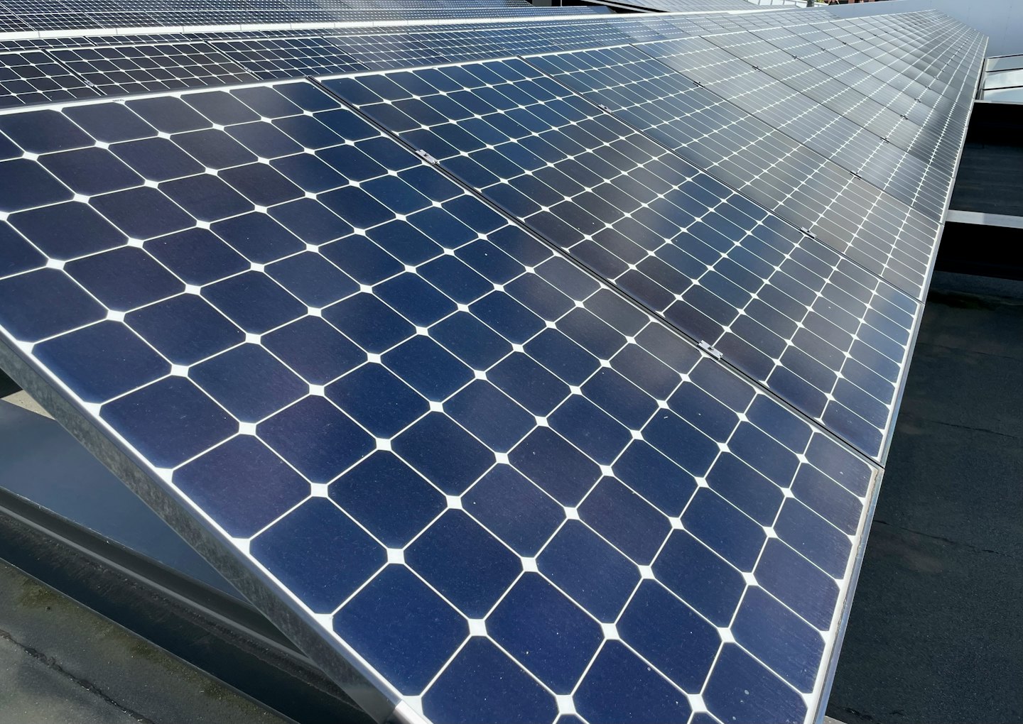 Paneles solares de color azul oscuro sobre un tejado negro bajo un cielo nublado.