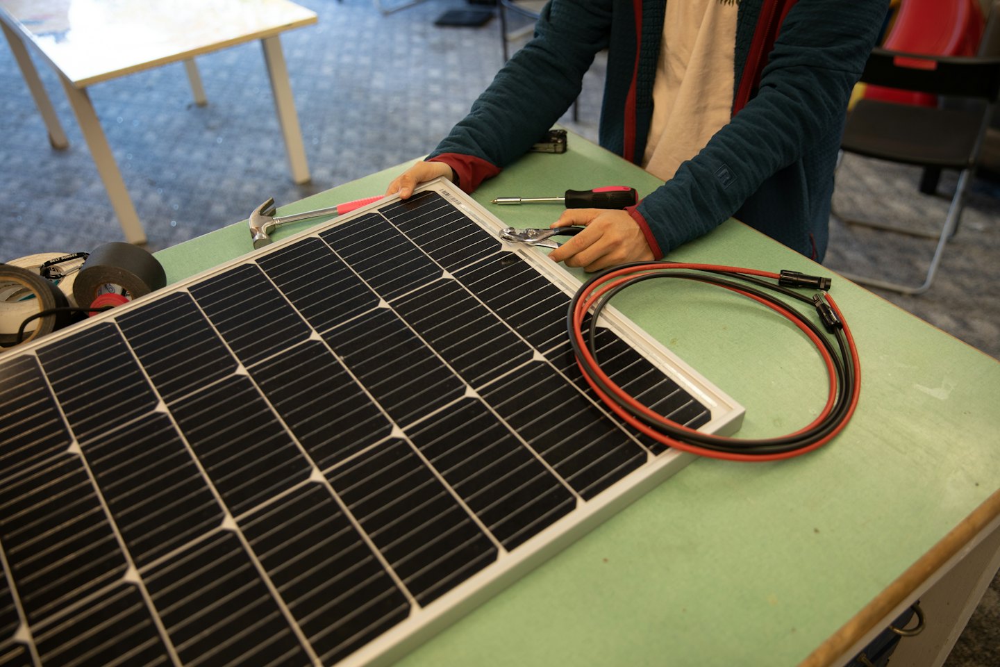 Un trabajador usa alicates para ensamblar un panel solar en un banco de trabajo.